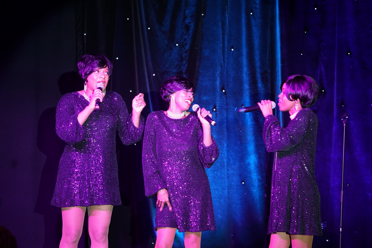 Three Motown Brunch singers in purple sequin dresses harmonizing live on stage in Las Vegas
